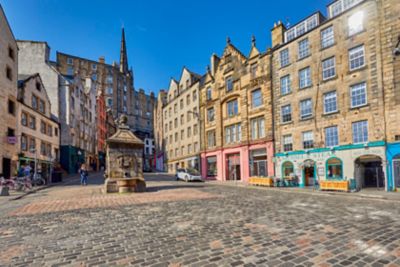 Grassmarket en Edimburgo, con edificios históricos y una fuente bajo el sol