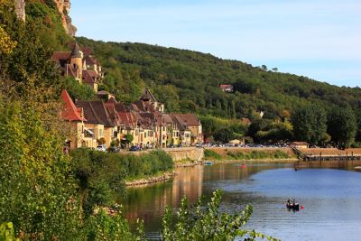 Houses on a riverbank, backed by forested cliffs, in La Roque-Gageac, Dordogne