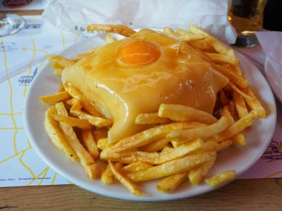 Un plato del sándwich típico francesinha de Oporto con huevo frito y patatas, cubierto de salsa