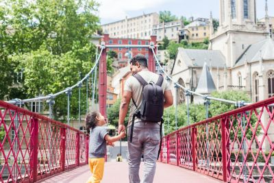 Padre e hija caminan de la mano cruzando un puente peatonal de color rojo