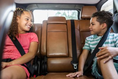 A pair of children smiling at each other in the back of a car