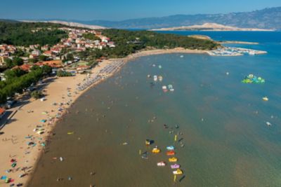 Rajska Plaža with a golden sand shore backed by pine trees and colourful boats in the water