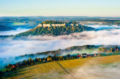 Nebelverhangene Festung Königstein nahe Dresden, die bei Sonnenaufgang über den Wolken thront