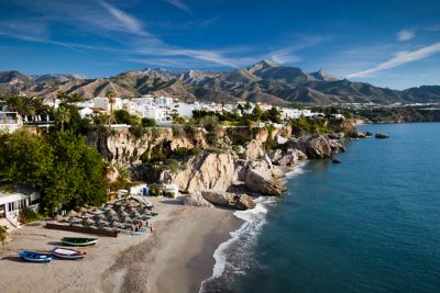Vista aérea de una playa en Nerja, con edificios blancos y montañas de fondo.