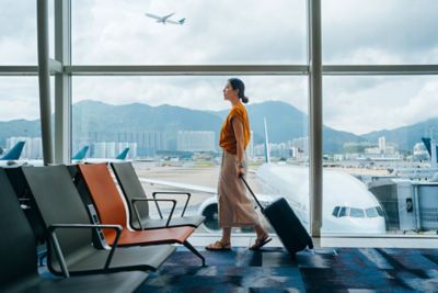 A relaxed traveller with a cabin bag strolling past a large airport window