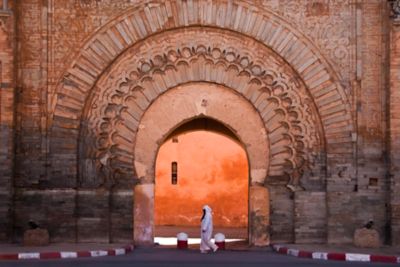 A veiled woman in front of the ornately carved, sandstone Bab Agnaou Gate in Marrakech