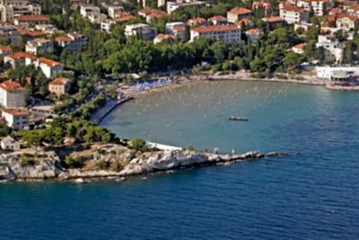 Crescent-shaped Bačvice Beach in Croatia with many swimmers in the water and blue umbrellas on the shore