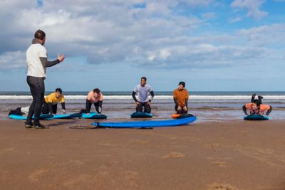 Instructor de surf dando clase a cinco alumnos con tablas azules en una playa