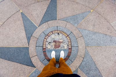 Persona de pie sobre la placa que indica el kilómetro cero, en la Puerta del Sol de Madrid
