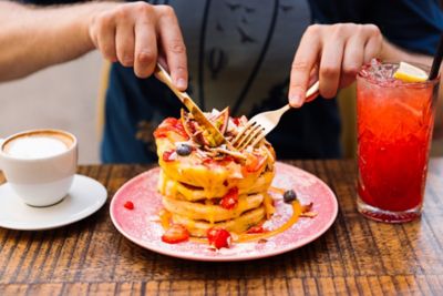 A restaurant diner cutting into a stack of pancakes topped with fruit and sauce