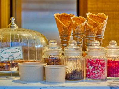 Waffle cones and glass bottles of colourful toppings at an ice-cream shop in France
