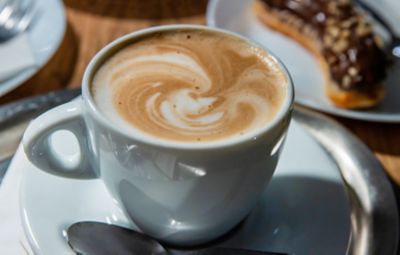 A latte with swirly foam in a white mug on a white saucer