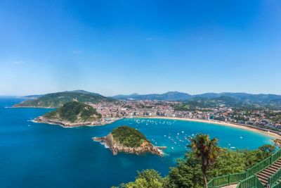 Vista aérea de la bahía de La Concha bajo un cielo azul despejado, con isla, ciudad y montañas