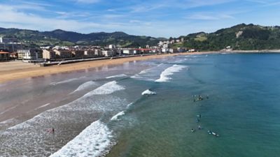 Extensa playa de arena dorada con surfistas y edificios costeros