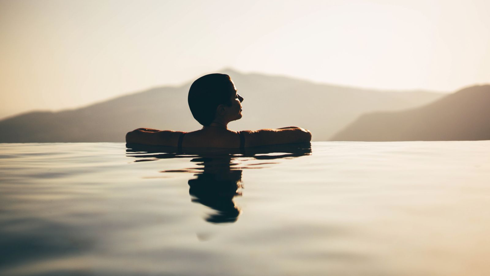A wellness seeker gazing over a calm mountain landscape from an infinity pool