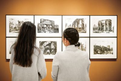 A pair of visitors discuss framed architectural drawings in an art gallery