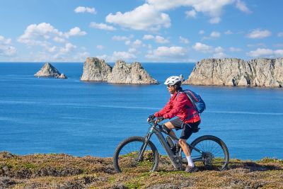 A cyclist on the rugged Finisterre coast in Brittany against the blue Atlantic Ocean