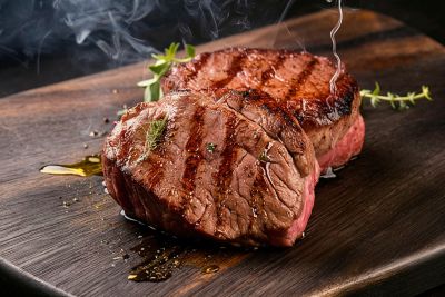 Thick-cut grilled steaks on a dark wooden board, garnished with thyme and olive oil