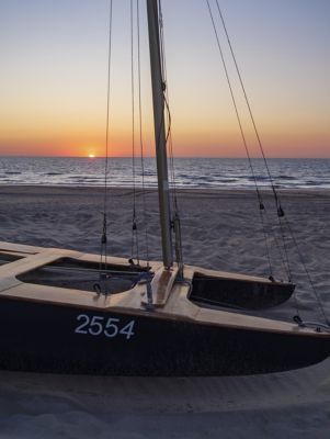A catamaran on sandy De Haan beach, Belgium, as the sun slips below the horizon