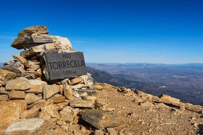 Señal que indica la cumbre del pico Torrecilla en un entorno montañoso bajo cielo azul