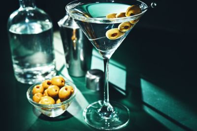 A dry martini with olives, plus a shaker, a bowl of olives and a bottle of gin