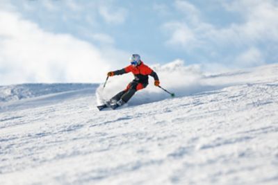 A teenager executing a carved turn while skiing down a snowy mountain