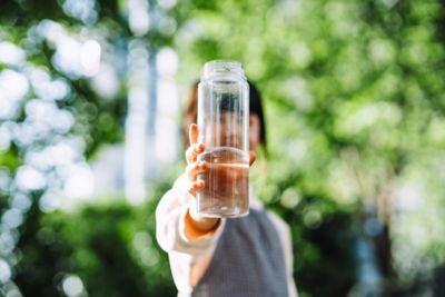 Une femme brandit une gourde d’eau transparente pour se réhydrater lors d’une promenade dans la forêt