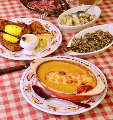 Mesa con mantel de cuadros rojos, platos con milanesa, lentejas, ensalada y suflé
