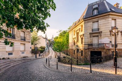 Calle empedrada curva en Montmartre, con edificios clásicos y la Basílica al fondo