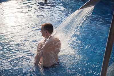 Hombre de espaldas en una piscina recibiendo un chorro de agua termal en los hombros