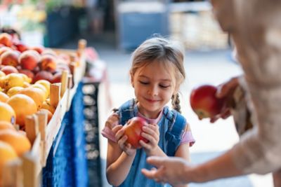 A child examining an apple at a market stall, ideal for sensory exploration