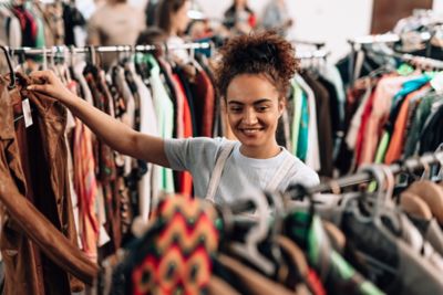 A smiling shopper holding up a pre-loved jacket in a vintage store