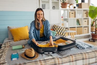 A happy traveller packing a small suitcase in a cosy bedroom at home
