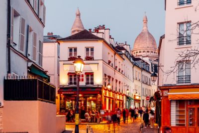 Passants et clients attablés à la terrasse d’un bistrot, dans une rue piétonne de Montmartre, en fin de journée