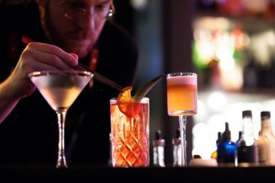A mixologist in a dimly lit bar creatively decorating a cocktail