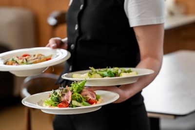 A server in a black-and-white uniform holding 3 plates in an elegant restaurant