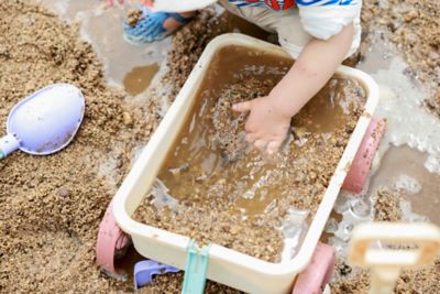 A preschooler's chubby hand immersed in a toy wagon of sand and water