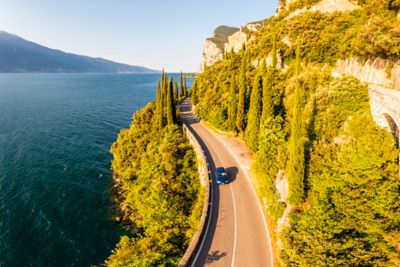 Une voiture bleue roule sur une route longeant le lac de Garde, lors d’un road trip en Italie