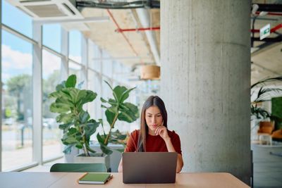Une femme qui semble absorbée par sa tâche sur son ordinateur portable, assise dans un espace de coworking