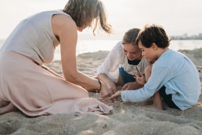 Une mère et ses deux enfants cherchent des coquillages dans le sable sur une plage en fin de journée