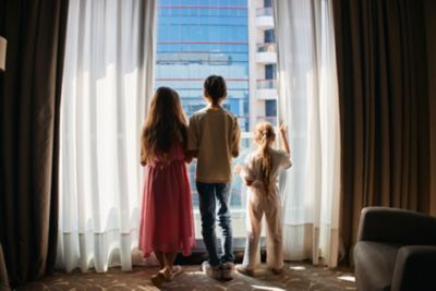 A trio of children gazing at the city view from their hotel window