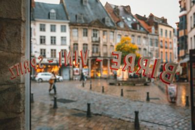 Blick durchs Glasfenster eines Estaminets in Lille hinaus auf eine Kopfsteinpflasterstraße im Regen
