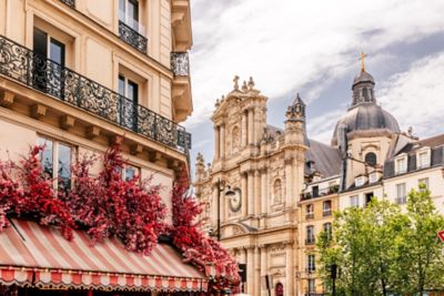 Calle parisina con fachadas clásicas, flores rojas y la cúpula de Saint-Paul-Saint-Louis al fondo