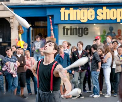 Straßenkünstler jongliert mit Keulen auf dem Edinburgh Festival Fringe vor Zuschauern im Hintergrund