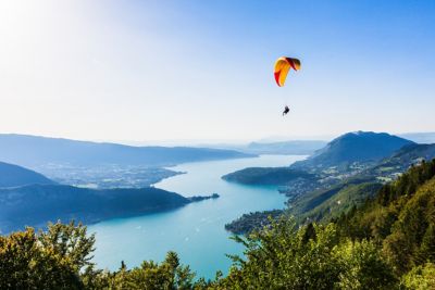 A lone paraglider high above Lake Annecy, France, against a misty blue sky