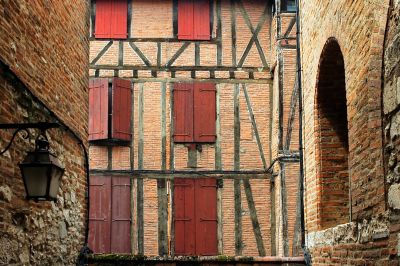 Façade d'une maison à colombages traditionnelle dans les ruelles du centre d’Albi, avec briques apparentes et volets rouges