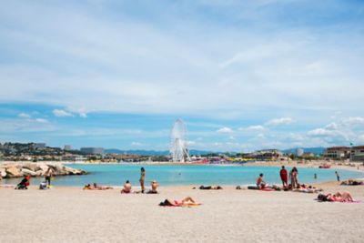 Sonnenbadende Menschen am Plage de Bonneveine in Marseille, mit Riesenrad im Hintergrund