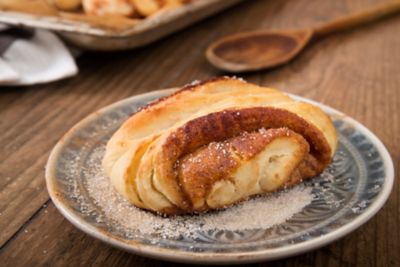 Reichlich mit Zucker bestäubtes Franzbrötchen auf rustikalem Tonteller