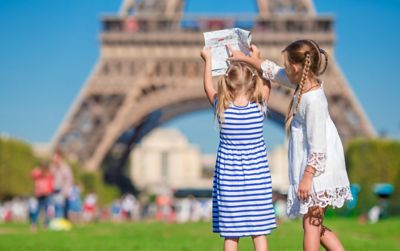 A pair of young children holding up a map in front of the Eiffel Tower, France