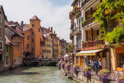 Buildings and purple flowers lining a canal on a sunny day in Annecy, France